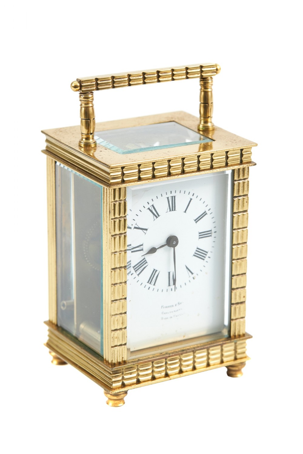 A rectangular brass carriage clock featuring bevelled glass side panels, a white enamel dial with black Roman numerals, textured corner pillars, and a hinged carrying handle.