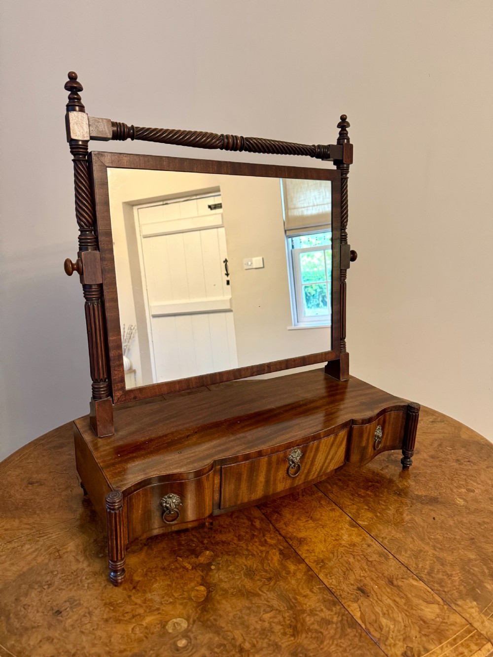 A Victorian mahogany swing mirror featuring a rectangular frame supported by spiral twist columns above a shaped base with three drawers and brass ring handles.