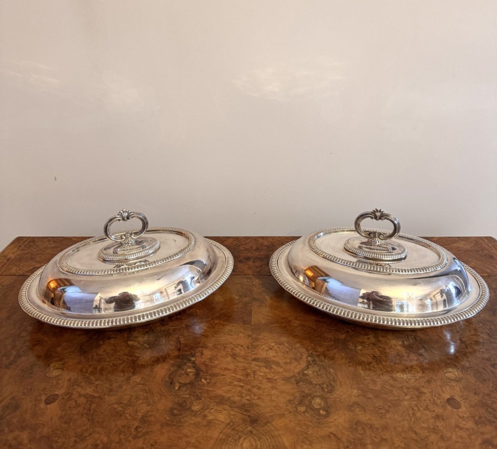 A pair of antique Edwardian oval silver-plated entree dishes featuring beaded borders and detachable loop handles.
