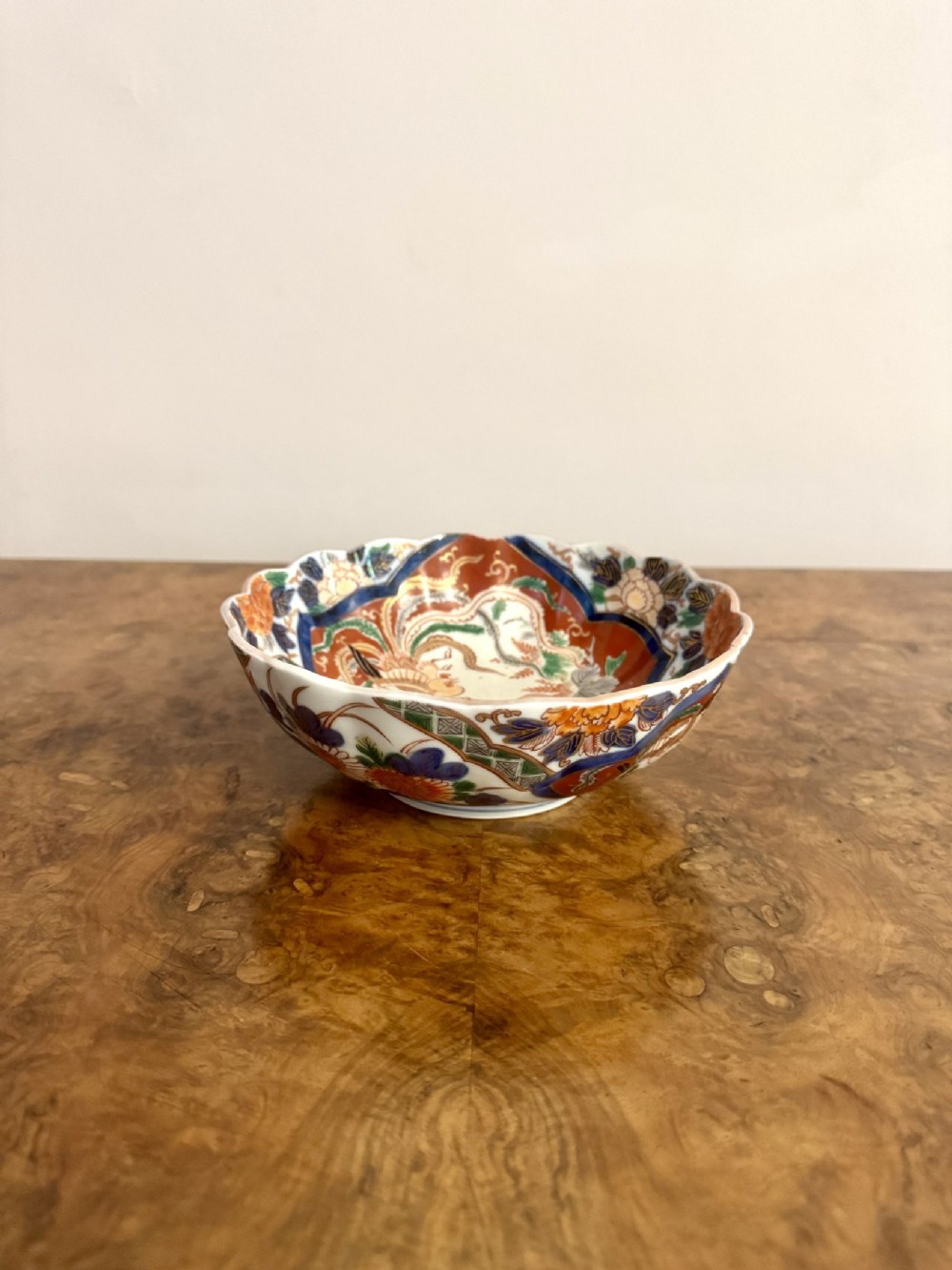 A small antique Japanese Imari porcelain bowl with a scalloped rim, hand-painted with iron-red, cobalt blue, and green floral panels.