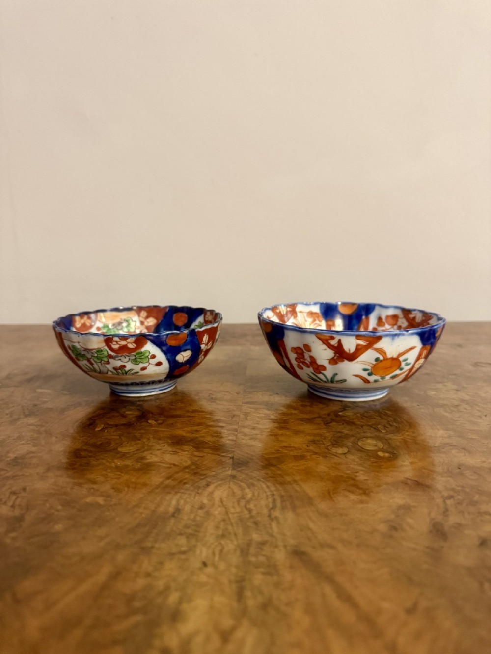 A pair of small Japanese Imari porcelain bowls with scalloped edges, hand-painted in cobalt blue, orange, and green floral motifs.