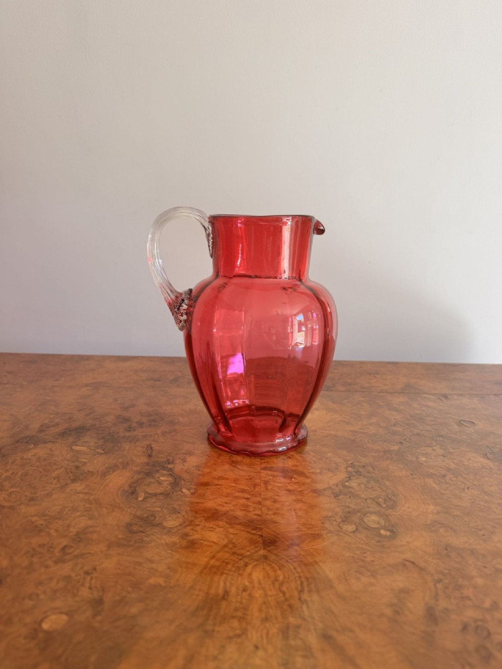 A Victorian cranberry red glass jug featuring a shaped body, flared neck, pouring spout, and an applied clear glass handle.