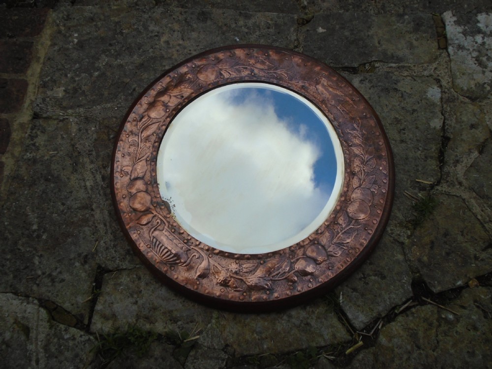 A circular antique Arts and Crafts copper wall mirror featuring hand-hammered repousse decoration of birds, foliage, and urns with a riveted border. View III