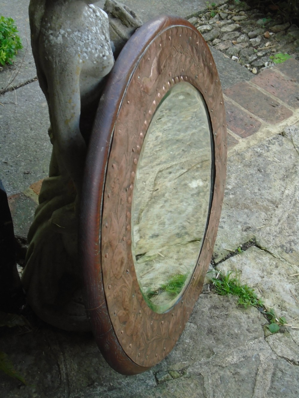 A circular antique Arts and Crafts copper wall mirror featuring hand-hammered repousse decoration of birds, foliage, and urns with a riveted border. View VII