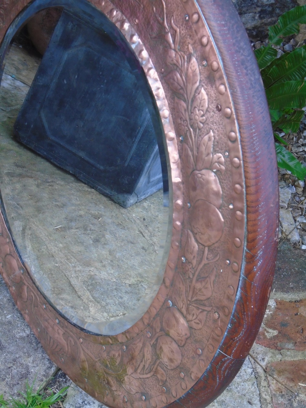 A circular antique Arts and Crafts copper wall mirror featuring hand-hammered repousse decoration of birds, foliage, and urns with a riveted border. View VIII