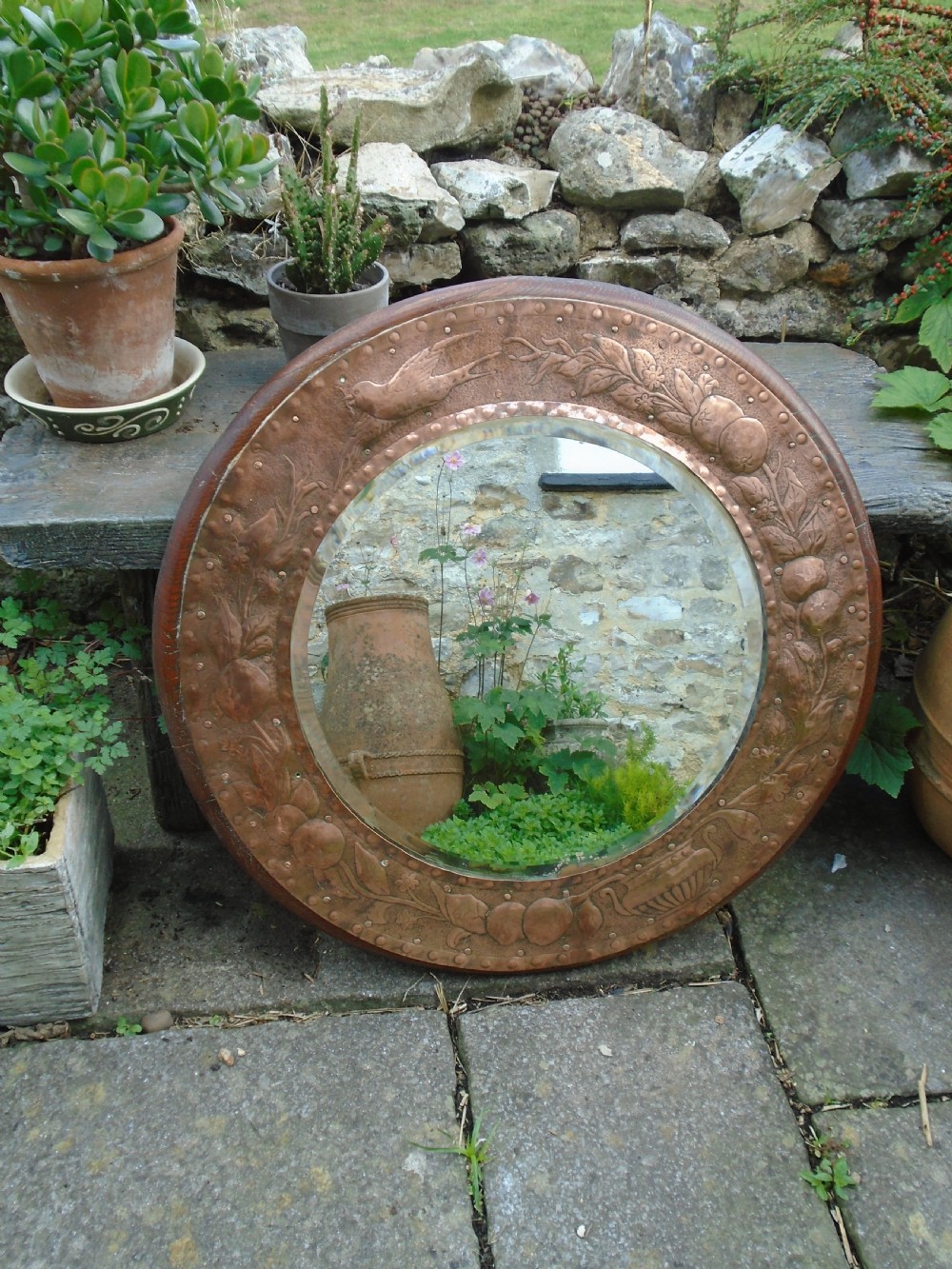 A circular antique Arts and Crafts copper wall mirror featuring hand-hammered repousse decoration of birds, foliage, and urns with a riveted border. View XI