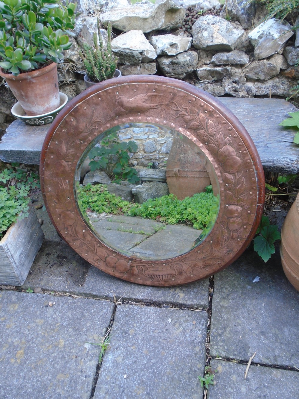 A circular antique Arts and Crafts copper wall mirror featuring hand-hammered repousse decoration of birds, foliage, and urns with a riveted border. View XIII