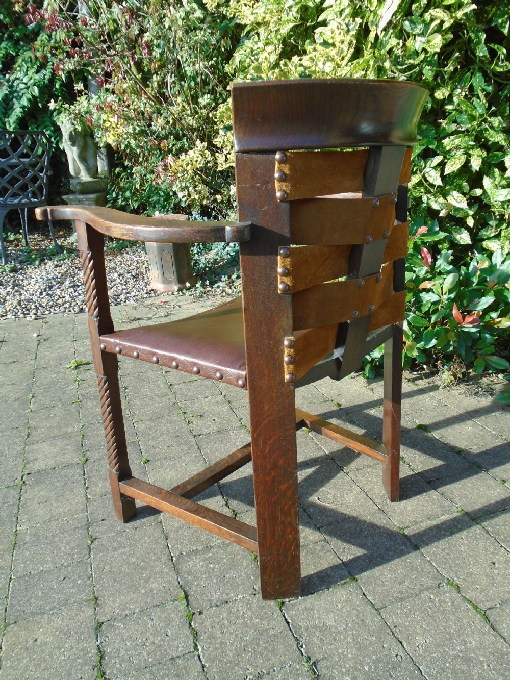 An Arts and Crafts solid oak armchair with carved spiral front legs, a brown leather seat secured with studs, and a curved slatted backrest. View III