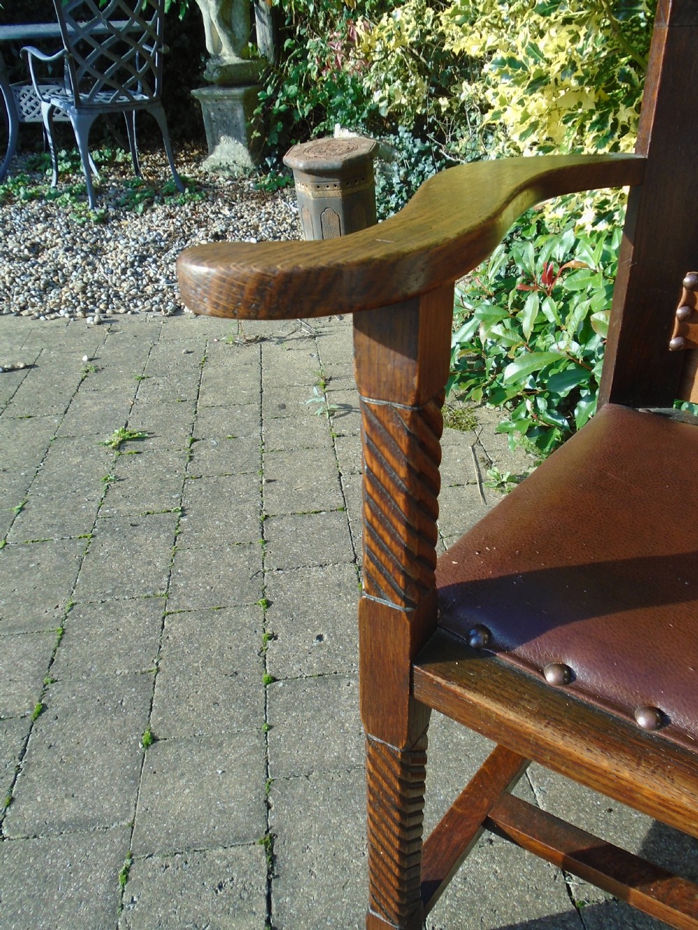 An Arts and Crafts solid oak armchair with carved spiral front legs, a brown leather seat secured with studs, and a curved slatted backrest. View IV