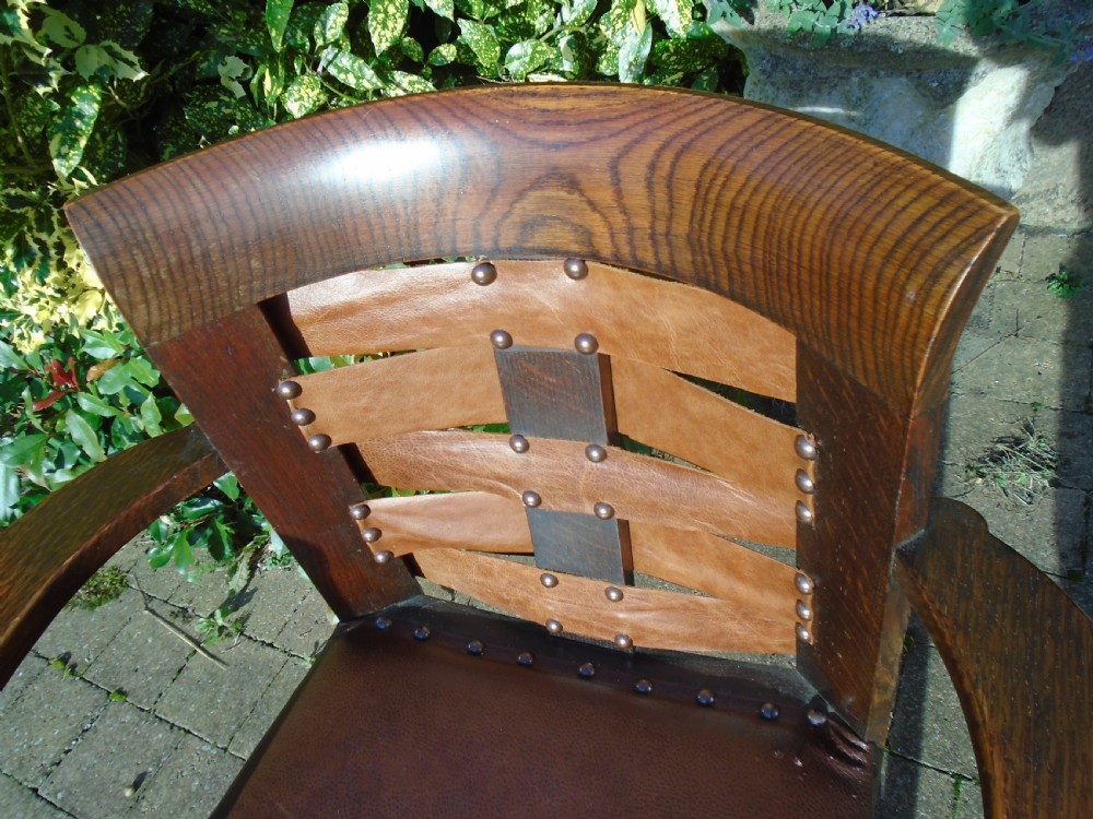 An Arts and Crafts solid oak armchair with carved spiral front legs, a brown leather seat secured with studs, and a curved slatted backrest. View VI