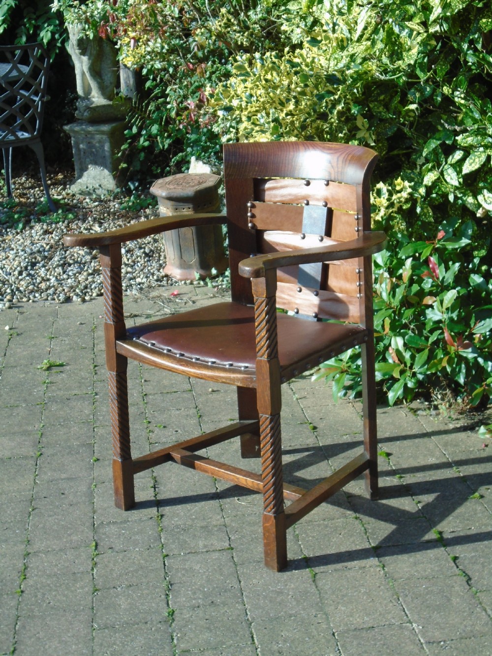 An Arts and Crafts solid oak armchair with carved spiral front legs, a brown leather seat secured with studs, and a curved slatted backrest. View VIII