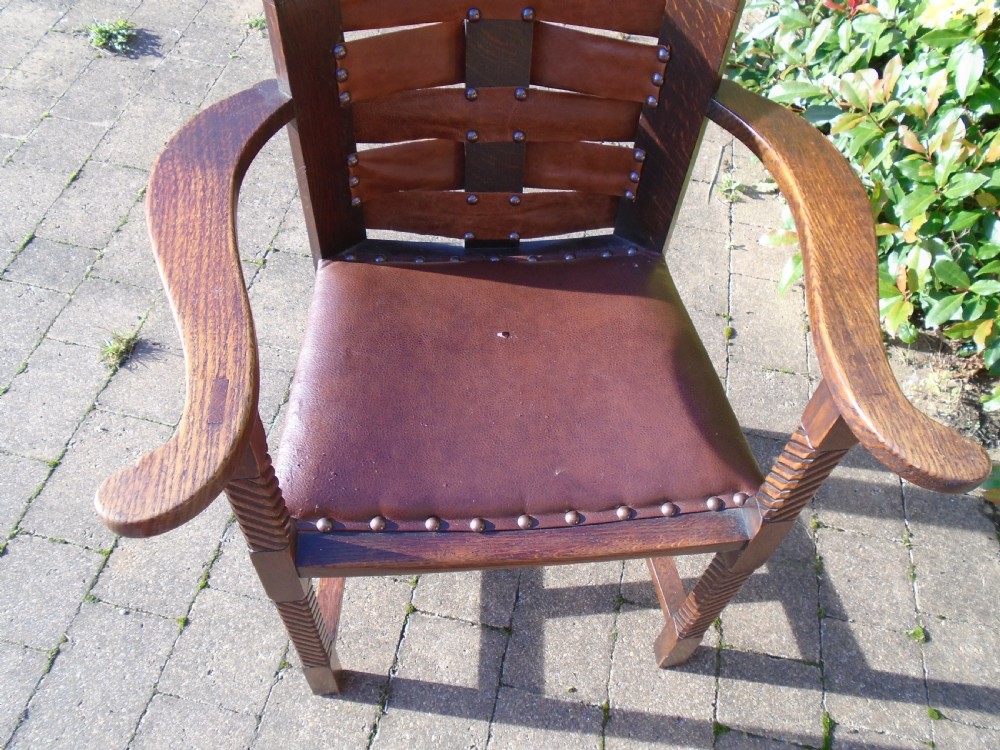 An Arts and Crafts solid oak armchair with carved spiral front legs, a brown leather seat secured with studs, and a curved slatted backrest. View IX