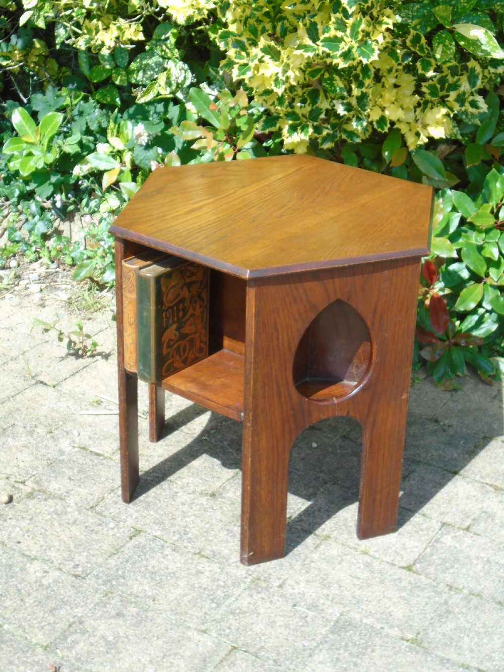 A hexagonal dark oak Arts and Crafts book table featuring teardrop cutouts on the legs and integrated book storage shelves. View II