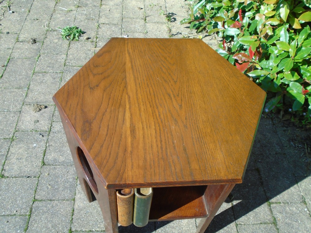 A hexagonal dark oak Arts and Crafts book table featuring teardrop cutouts on the legs and integrated book storage shelves. View III