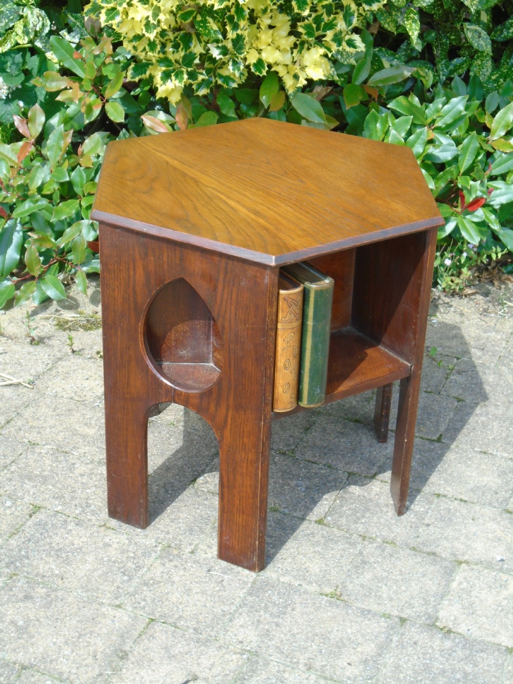 A hexagonal dark oak Arts and Crafts book table featuring teardrop cutouts on the legs and integrated book storage shelves. View IV