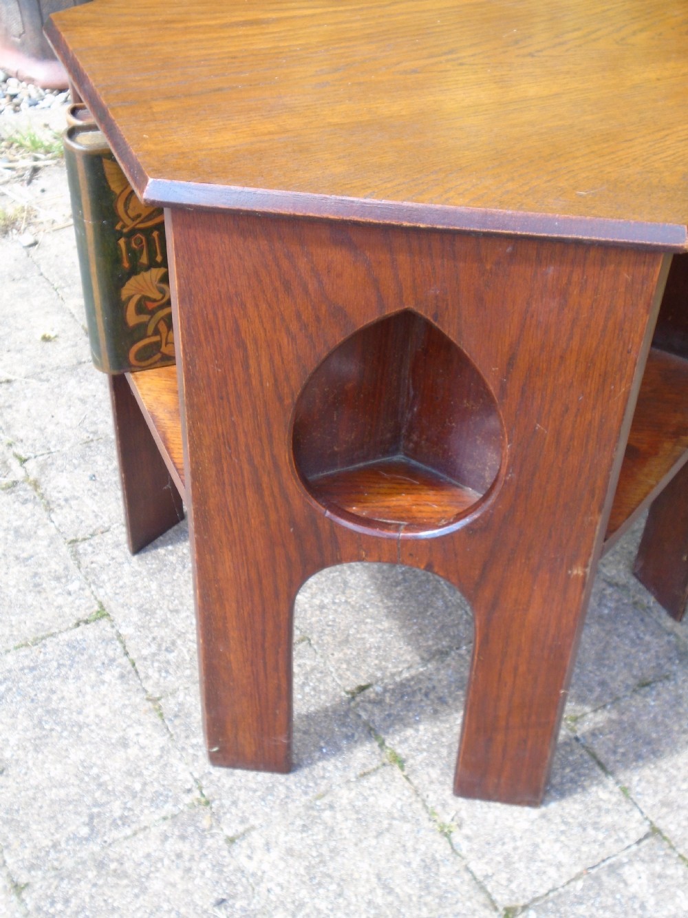 A hexagonal dark oak Arts and Crafts book table featuring teardrop cutouts on the legs and integrated book storage shelves. View V