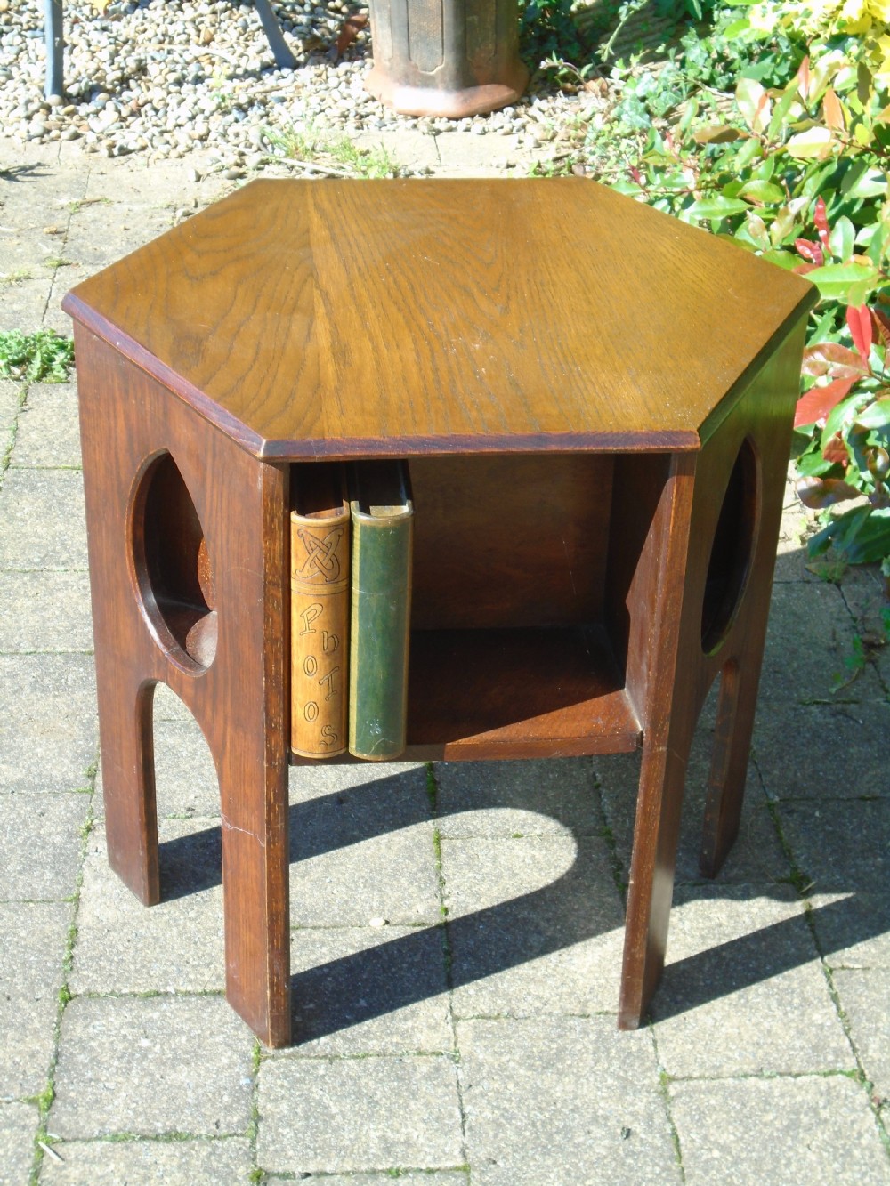 A hexagonal dark oak Arts and Crafts book table featuring teardrop cutouts on the legs and integrated book storage shelves. View VI