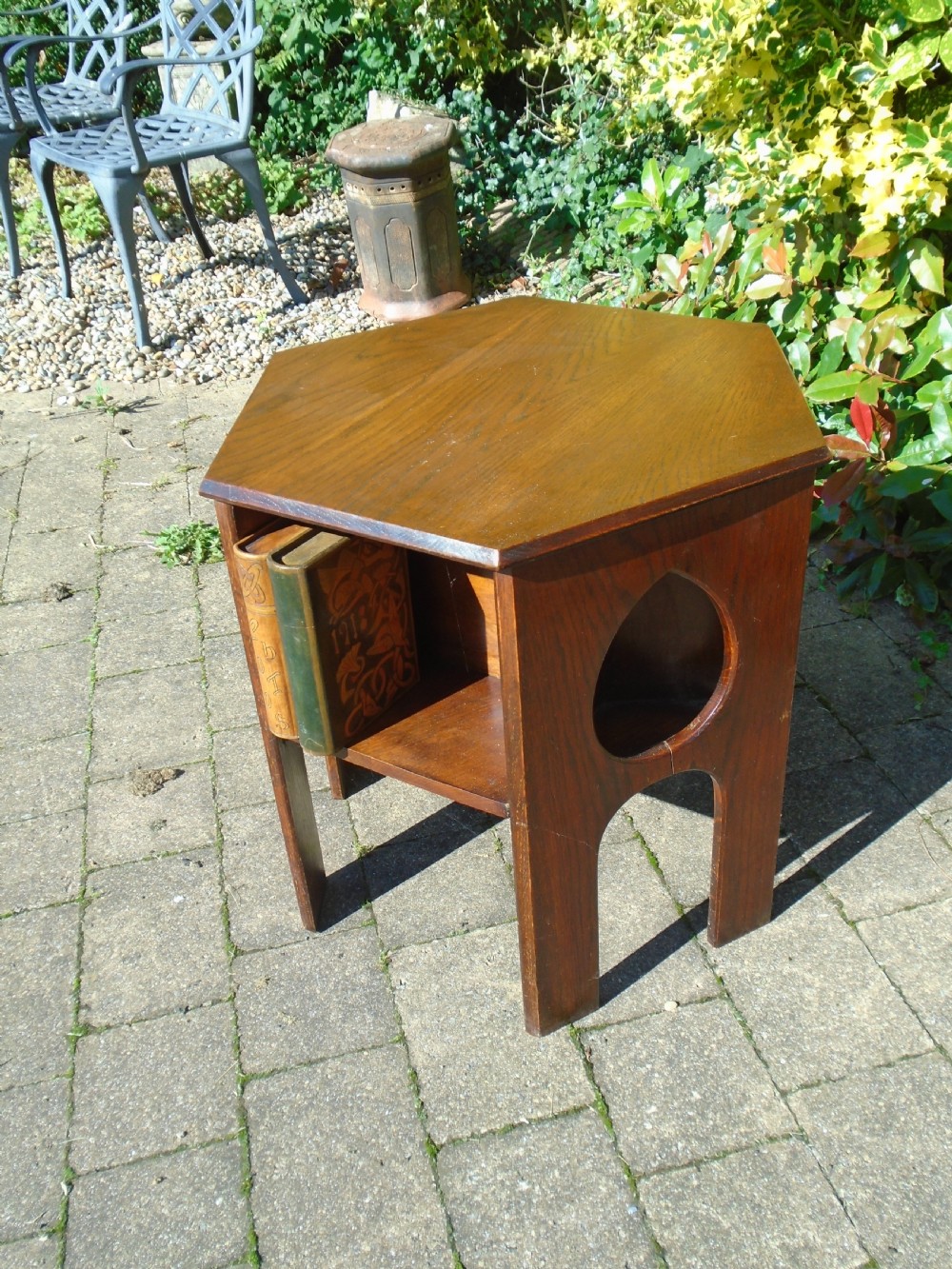 A hexagonal dark oak Arts and Crafts book table featuring teardrop cutouts on the legs and integrated book storage shelves. View VII