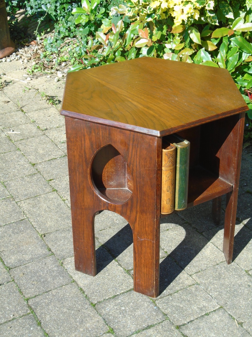 A hexagonal dark oak Arts and Crafts book table featuring teardrop cutouts on the legs and integrated book storage shelves. View VIII