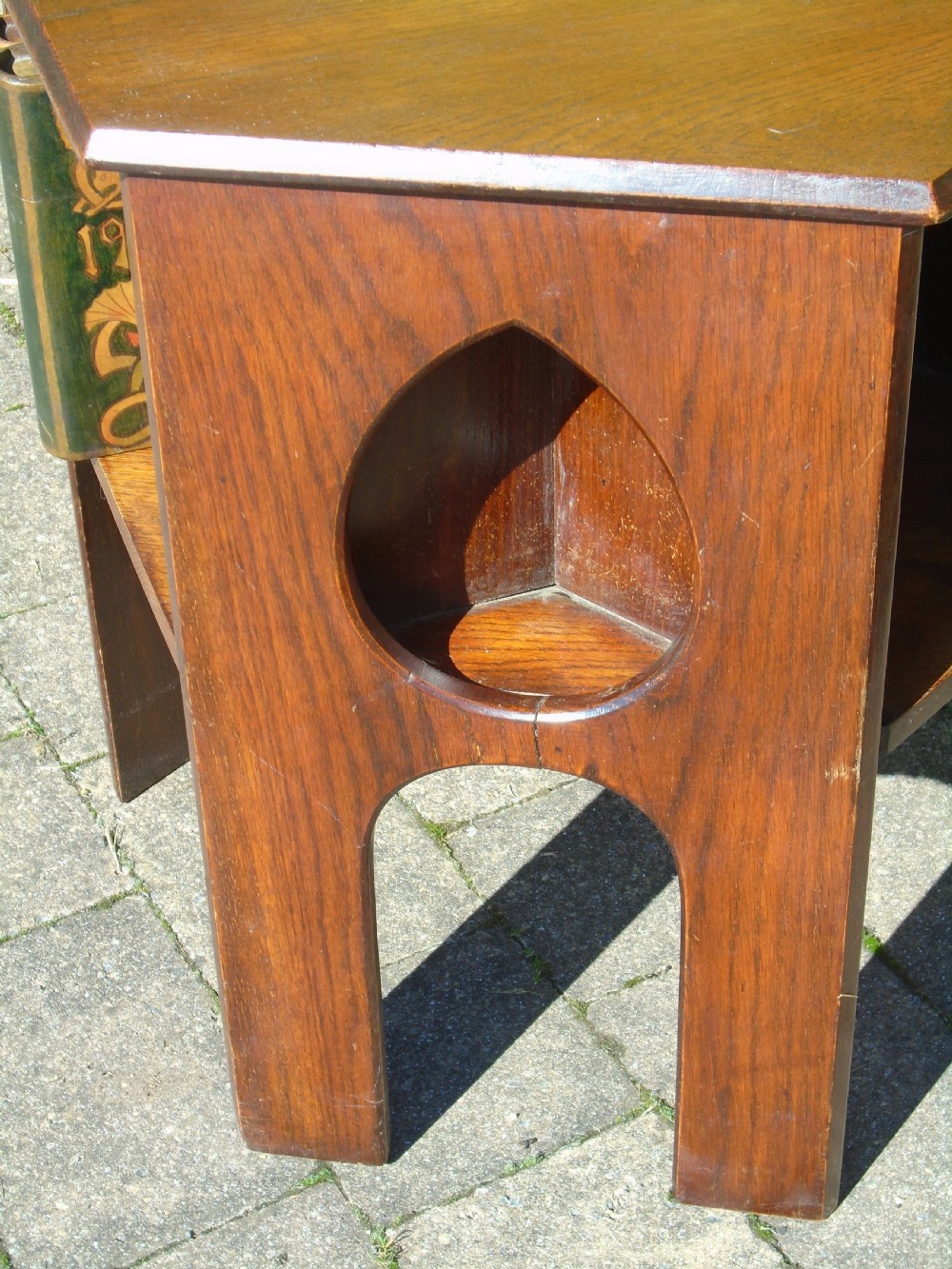 A hexagonal dark oak Arts and Crafts book table featuring teardrop cutouts on the legs and integrated book storage shelves. View IX