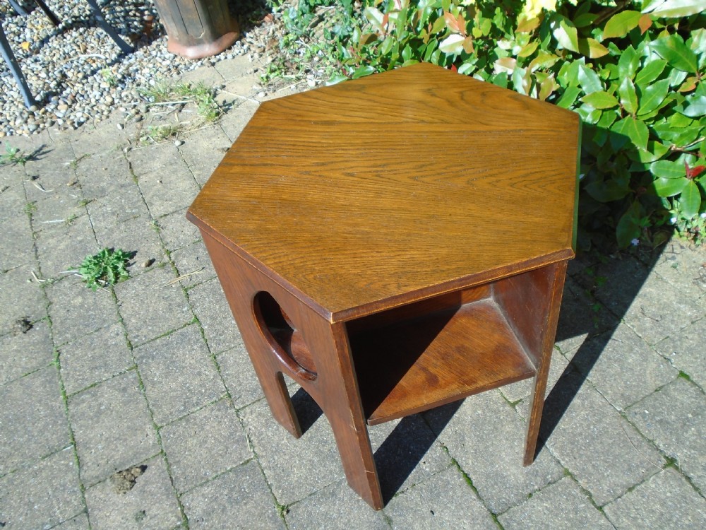 A hexagonal dark oak Arts and Crafts book table featuring teardrop cutouts on the legs and integrated book storage shelves. View X