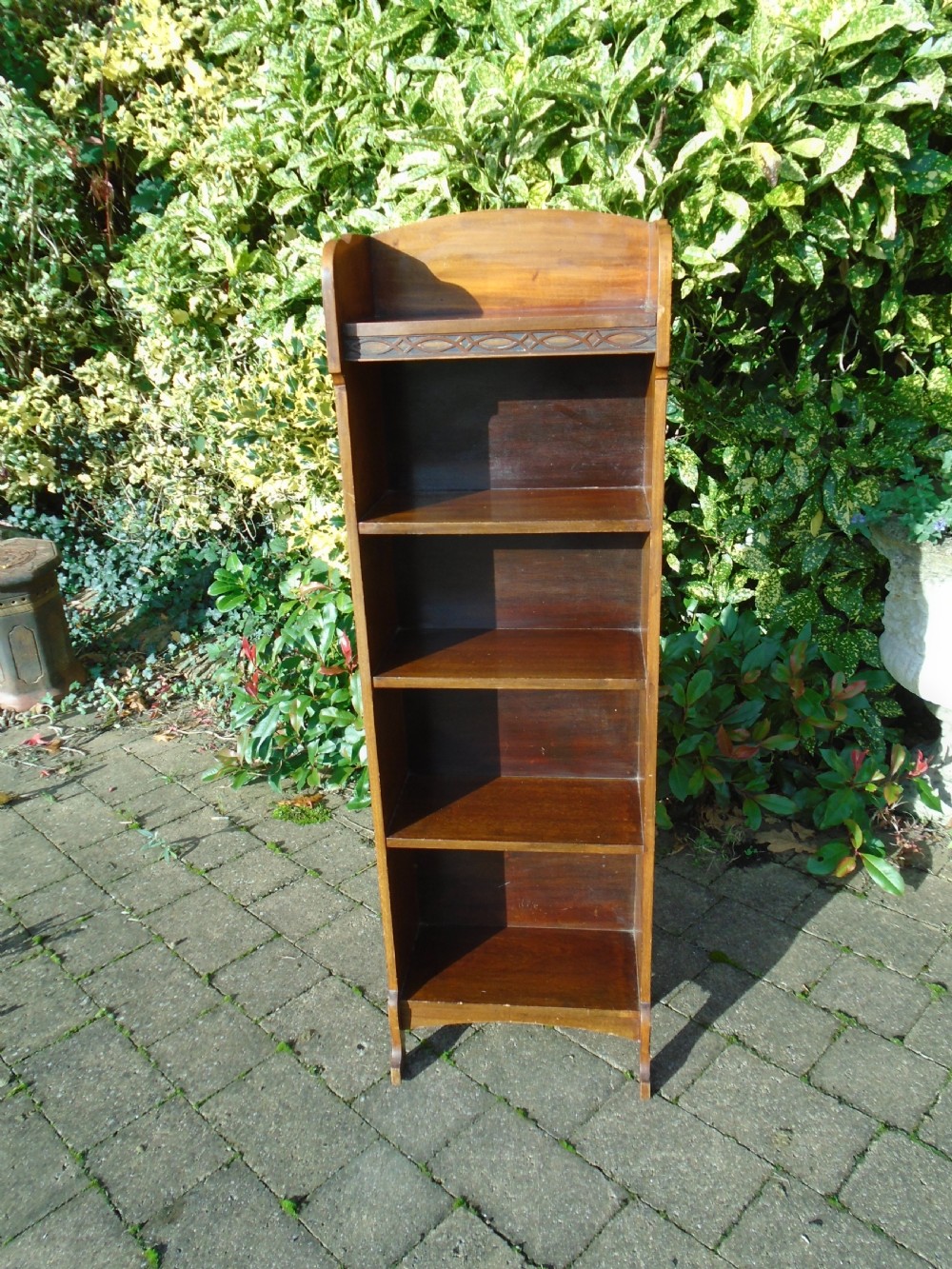 A tall, narrow Arts and Crafts walnut open bookcase featuring four shelves and carved decorative details along the upper frieze. View II