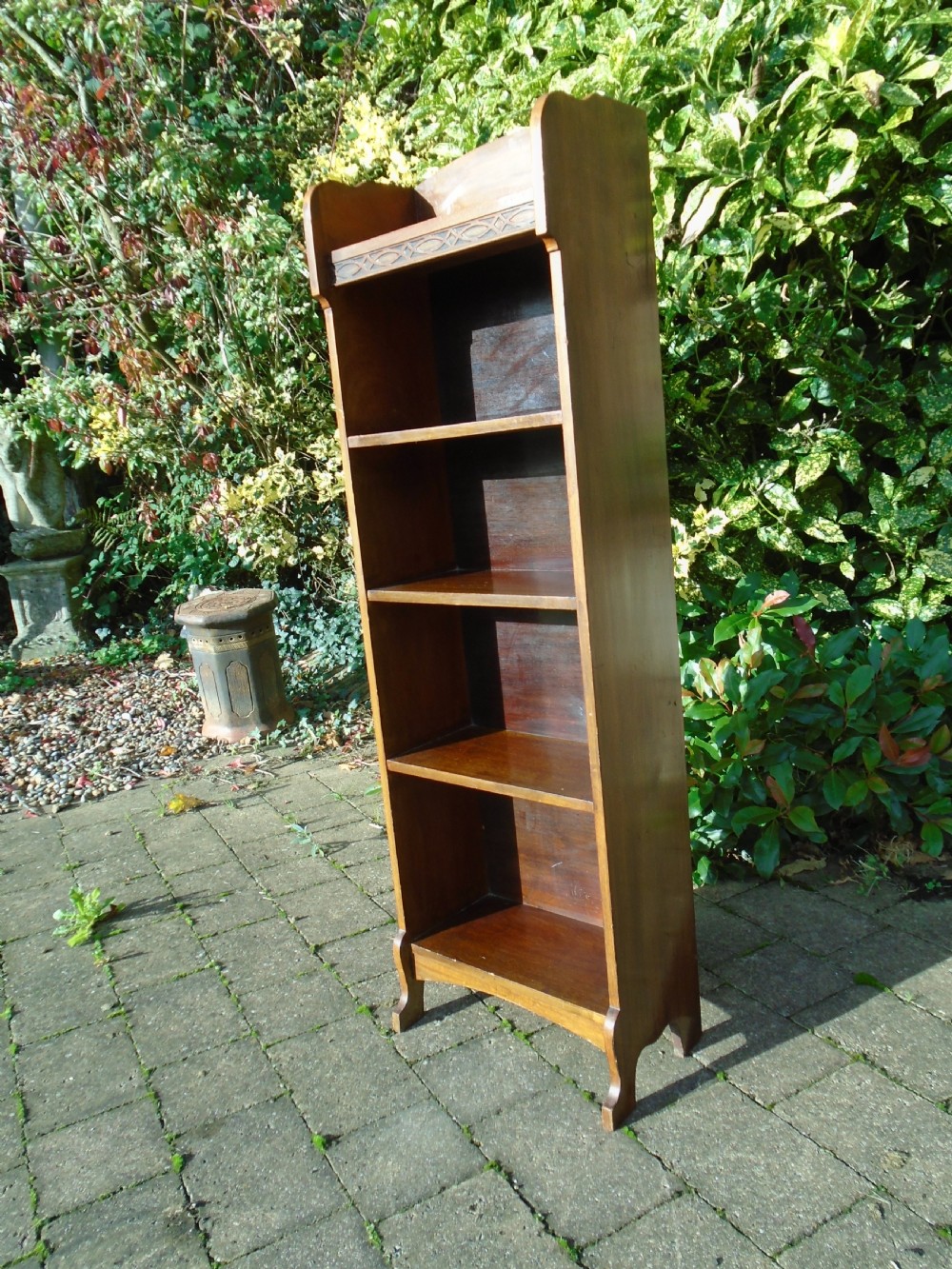 A tall, narrow Arts and Crafts walnut open bookcase featuring four shelves and carved decorative details along the upper frieze. View V