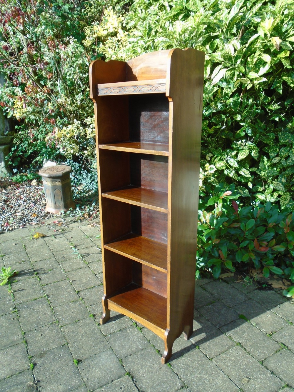 A tall, narrow Arts and Crafts walnut open bookcase featuring four shelves and carved decorative details along the upper frieze. View VI