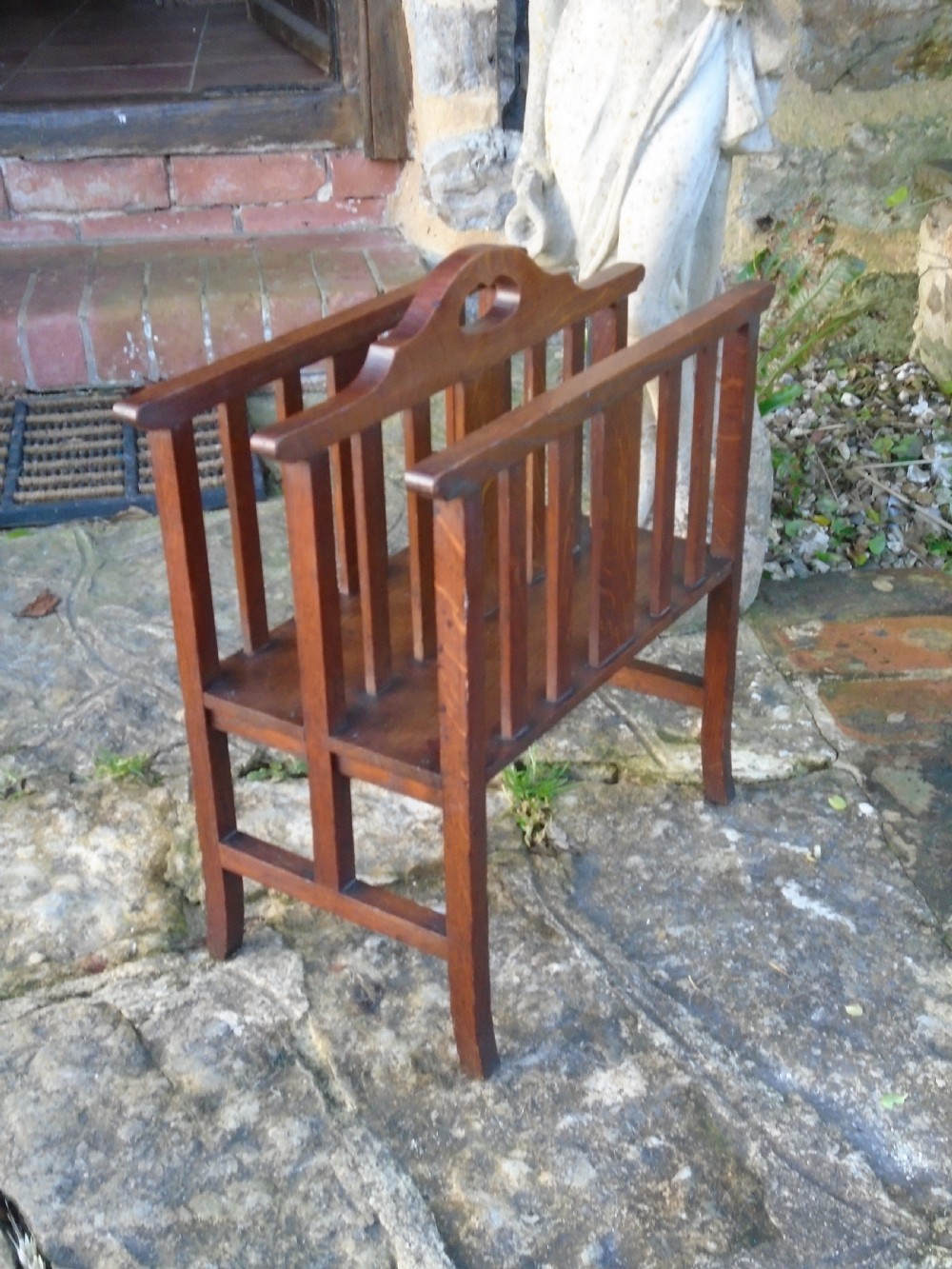 An Arts and Crafts solid oak magazine rack featuring vertical slatted sides, two compartments, and a central shaped divider with a heart cutout handle. View III