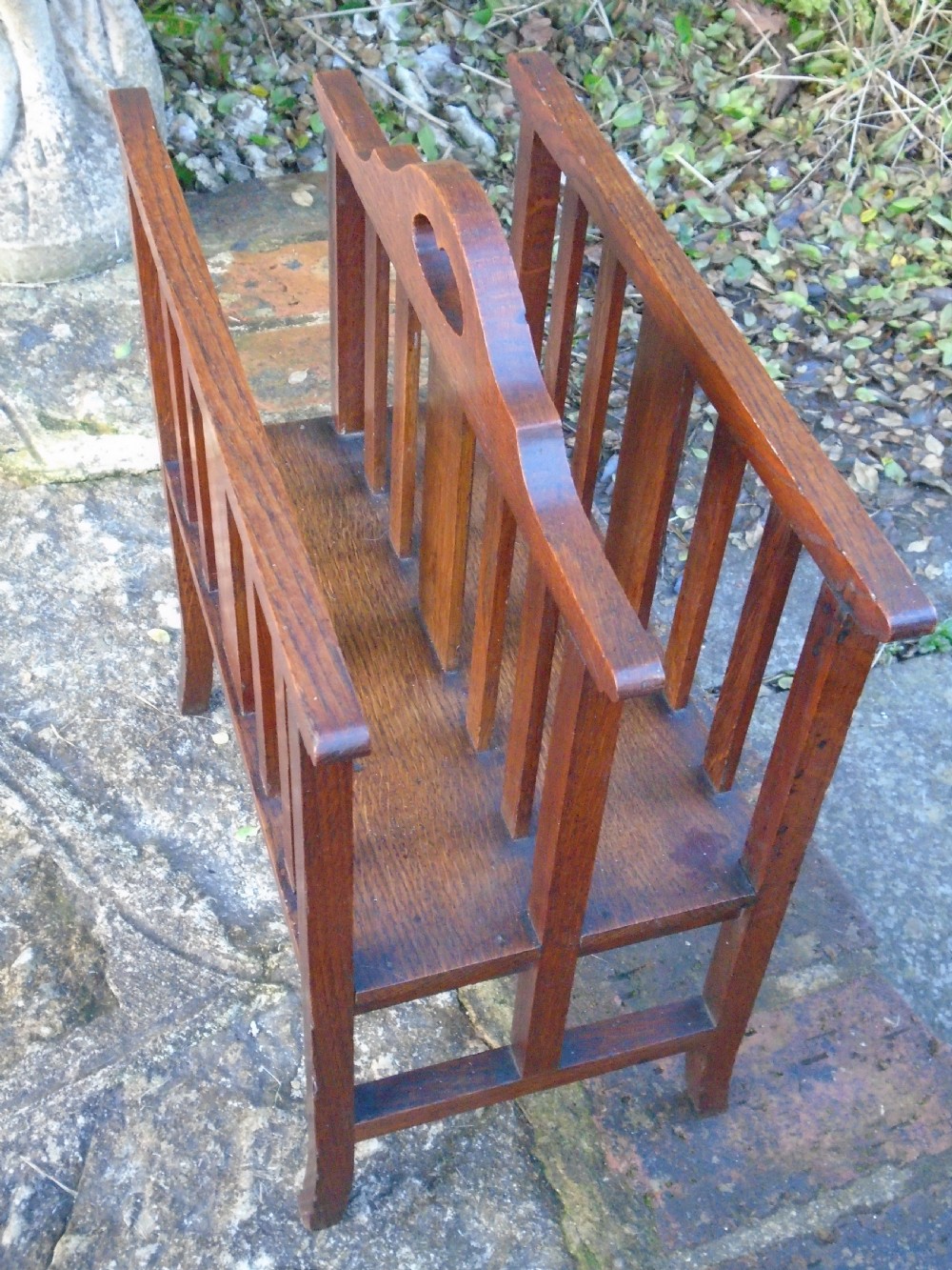 An Arts and Crafts solid oak magazine rack featuring vertical slatted sides, two compartments, and a central shaped divider with a heart cutout handle. View IV