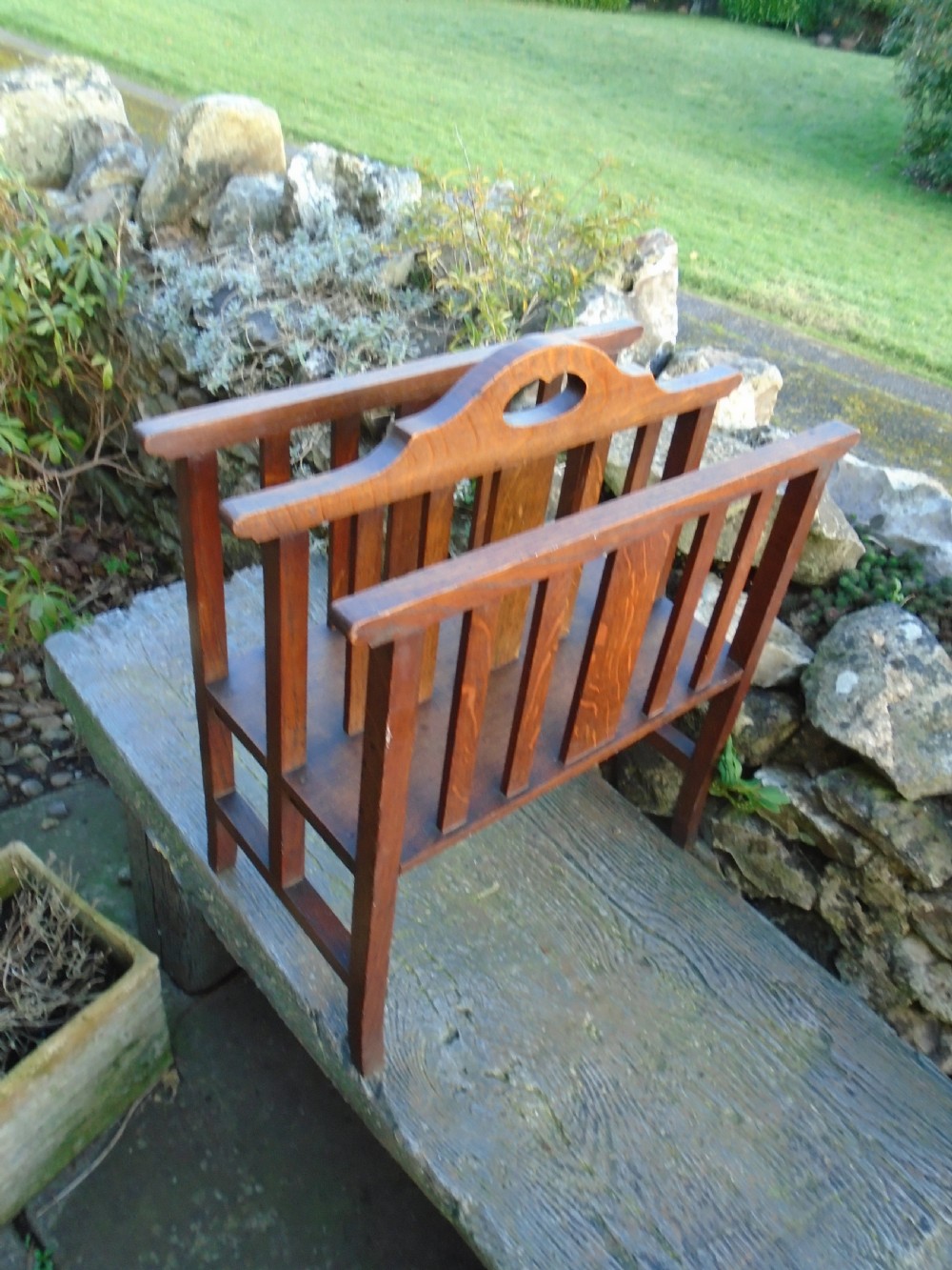 An Arts and Crafts solid oak magazine rack featuring vertical slatted sides, two compartments, and a central shaped divider with a heart cutout handle. View V