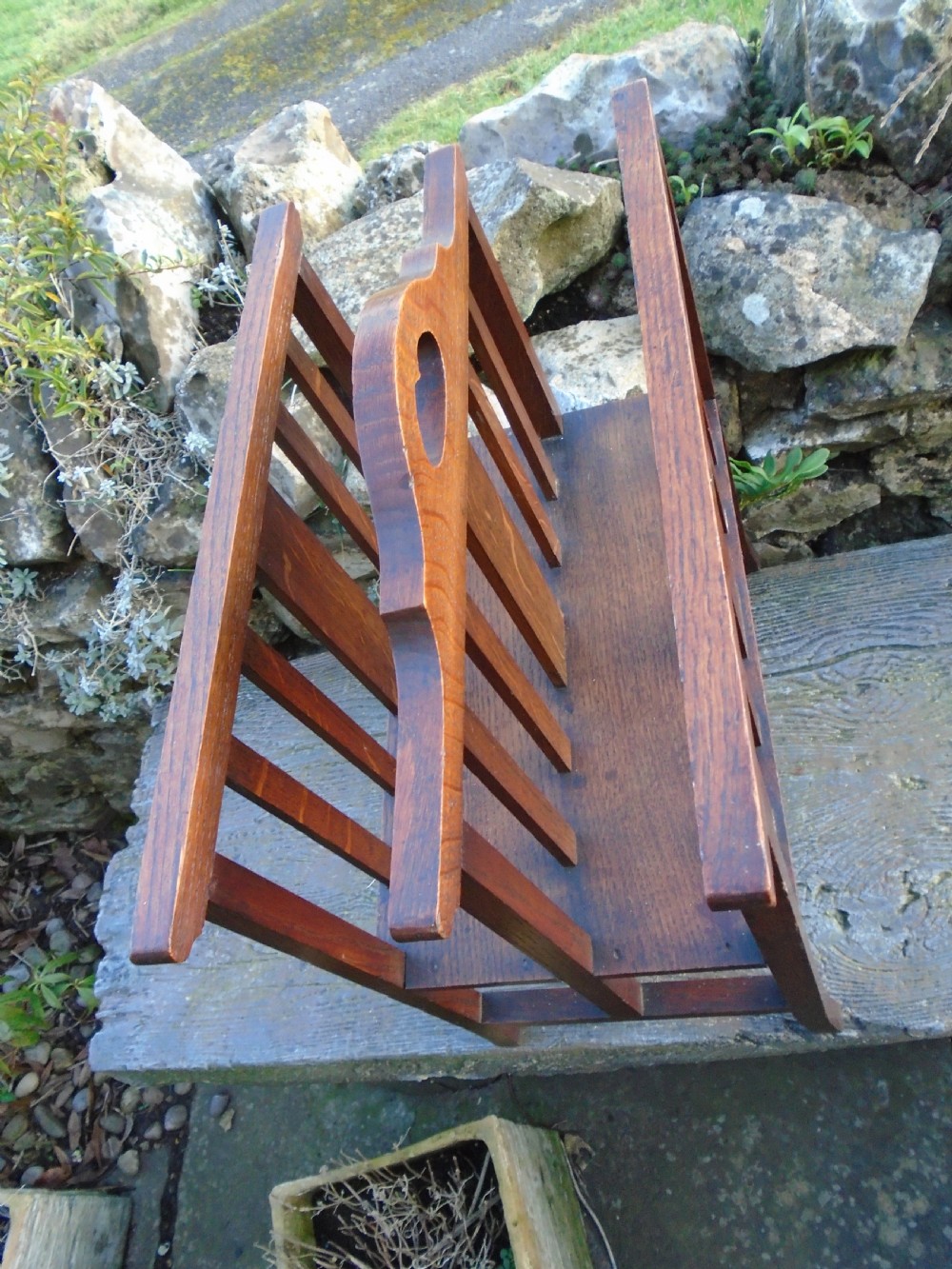 An Arts and Crafts solid oak magazine rack featuring vertical slatted sides, two compartments, and a central shaped divider with a heart cutout handle. View VI