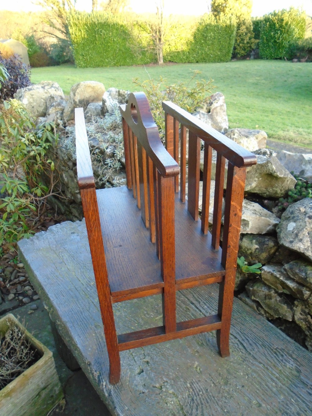 An Arts and Crafts solid oak magazine rack featuring vertical slatted sides, two compartments, and a central shaped divider with a heart cutout handle. View IX