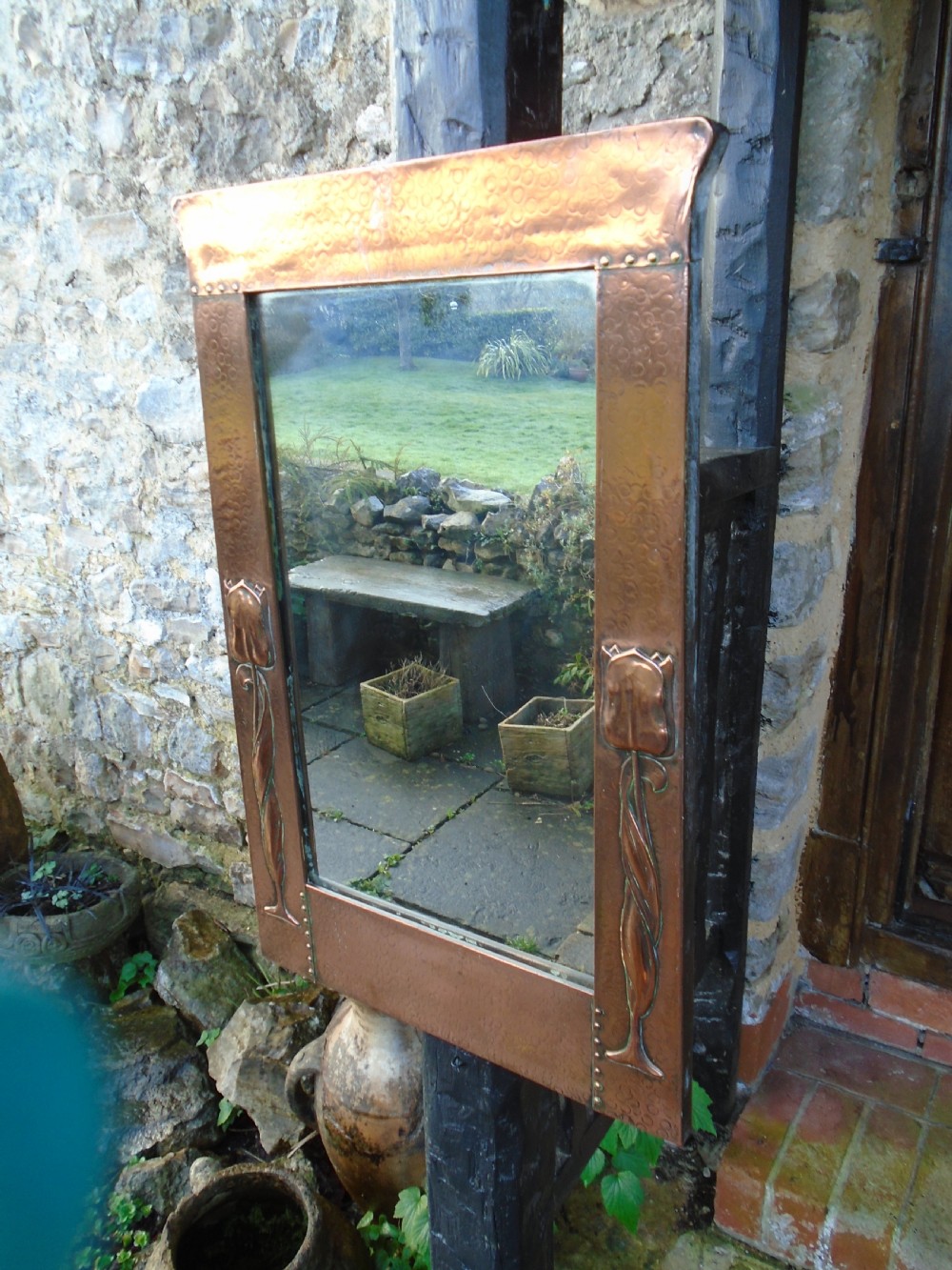A rectangular Arts and Crafts wall mirror featuring a beaten copper frame with riveted corners and embossed tulip motifs along the side panels. View II