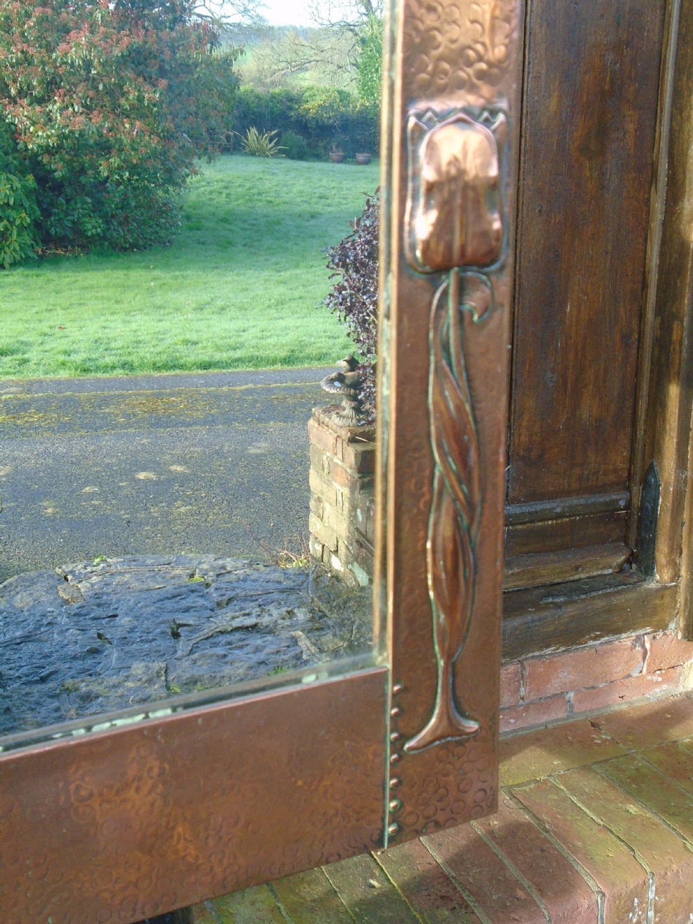 A rectangular Arts and Crafts wall mirror featuring a beaten copper frame with riveted corners and embossed tulip motifs along the side panels. View III