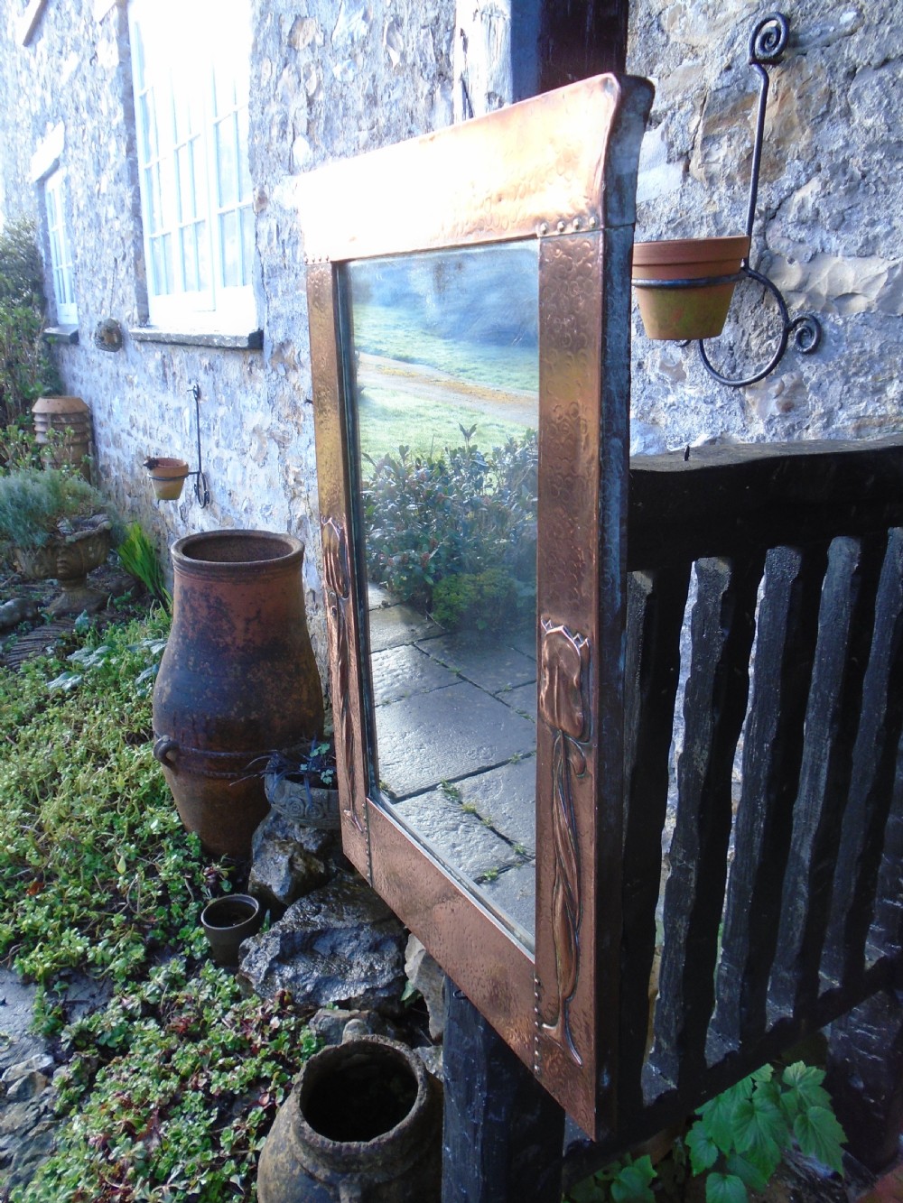 A rectangular Arts and Crafts wall mirror featuring a beaten copper frame with riveted corners and embossed tulip motifs along the side panels. View IV