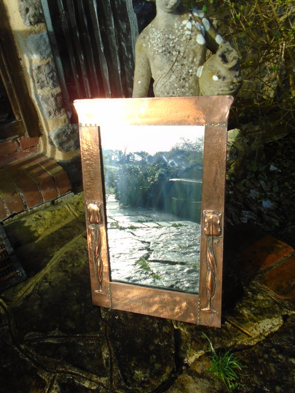 A rectangular Arts and Crafts wall mirror featuring a beaten copper frame with riveted corners and embossed tulip motifs along the side panels. View V
