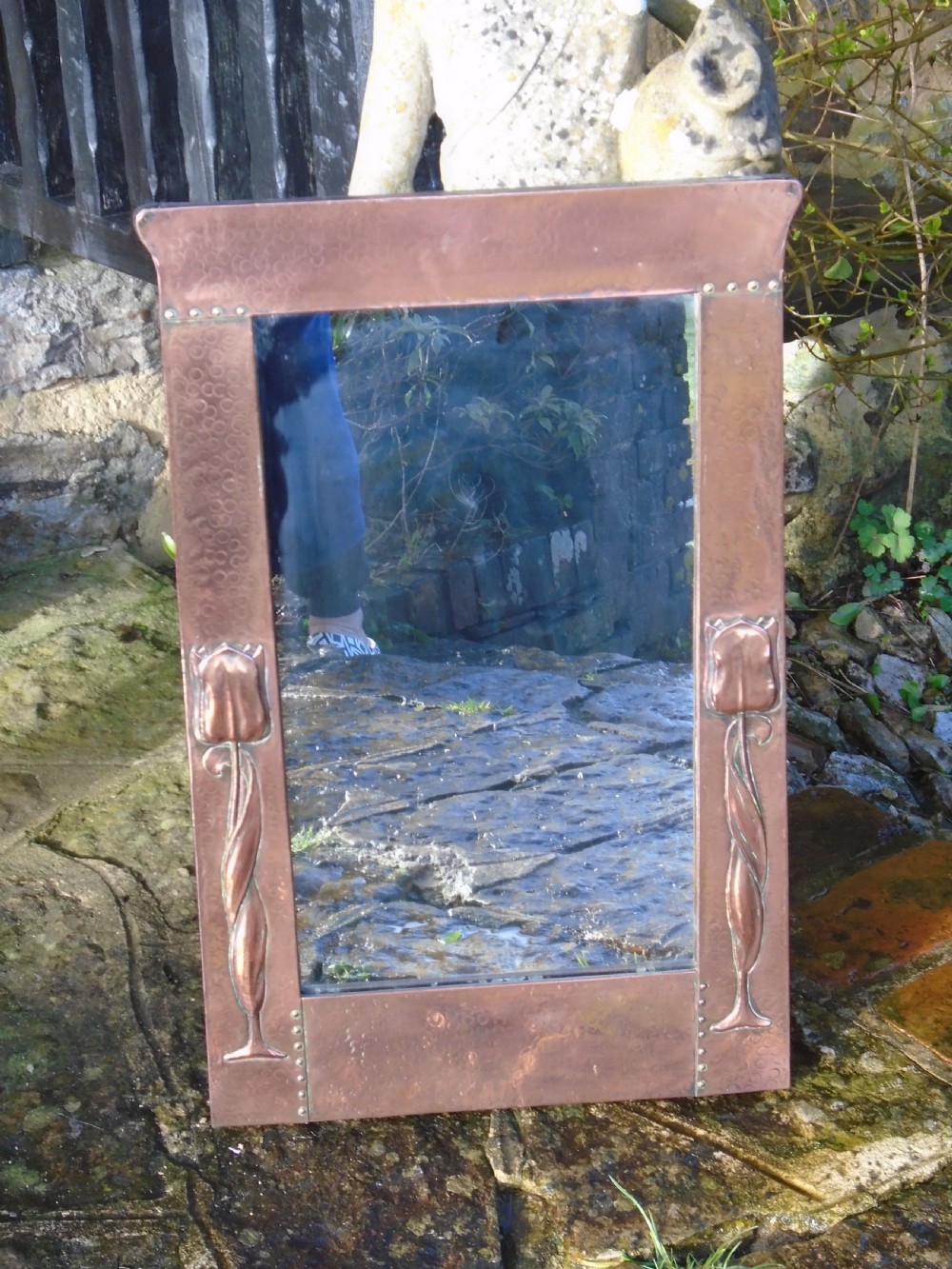 A rectangular Arts and Crafts wall mirror featuring a beaten copper frame with riveted corners and embossed tulip motifs along the side panels. View VII