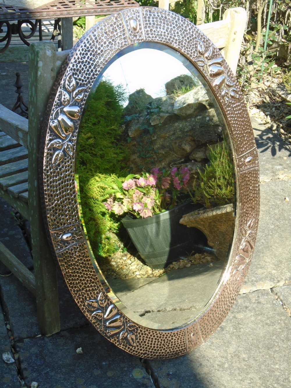 An oval Arts and Crafts mirror featuring a hand-hammered copper frame decorated with embossed pear motifs and decorative raised cabochons.