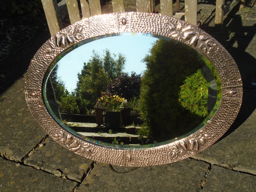 An oval Arts and Crafts mirror featuring a hand-hammered copper frame decorated with embossed pear motifs and decorative raised cabochons. View II