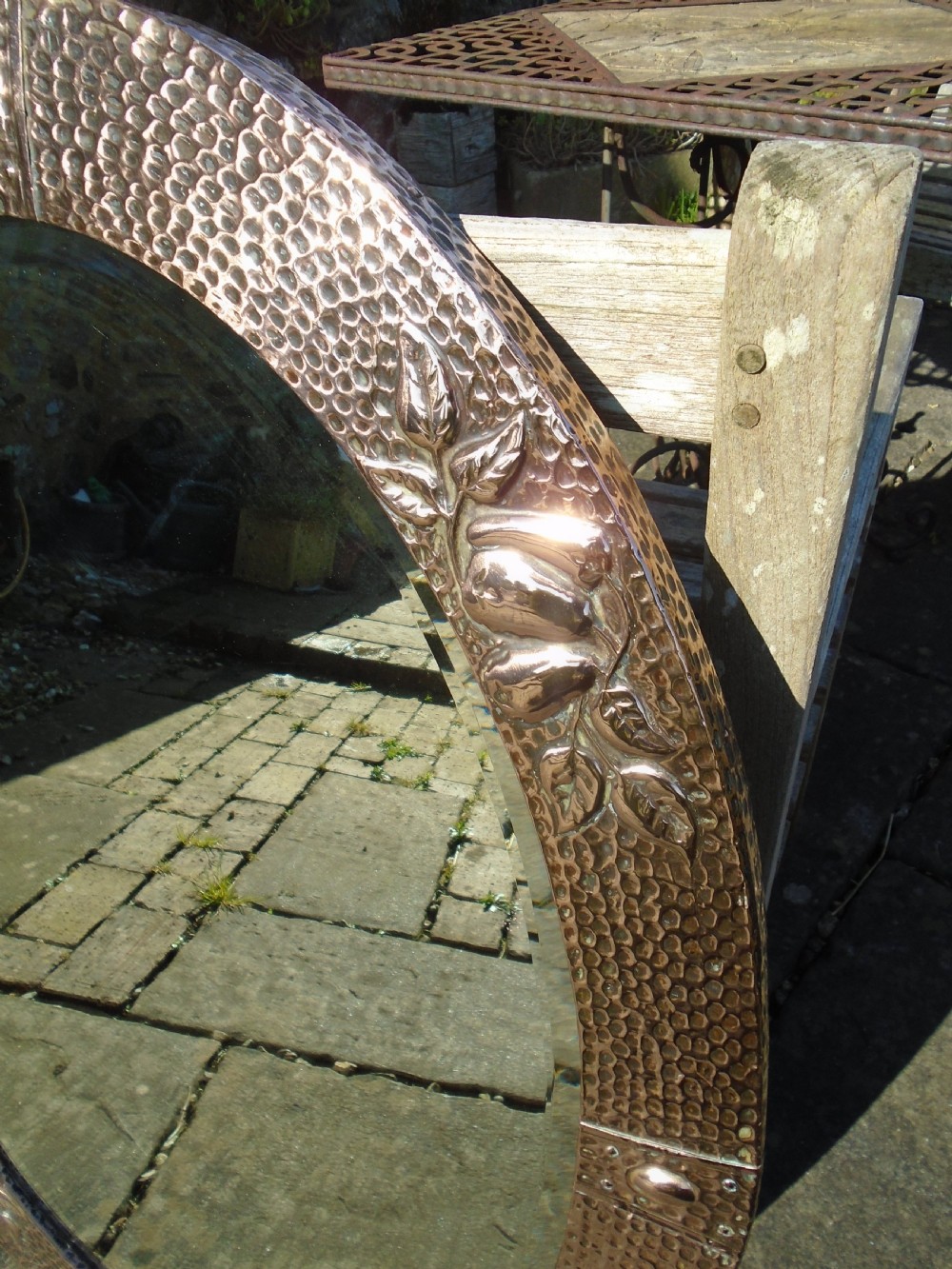 An oval Arts and Crafts mirror featuring a hand-hammered copper frame decorated with embossed pear motifs and decorative raised cabochons. View III