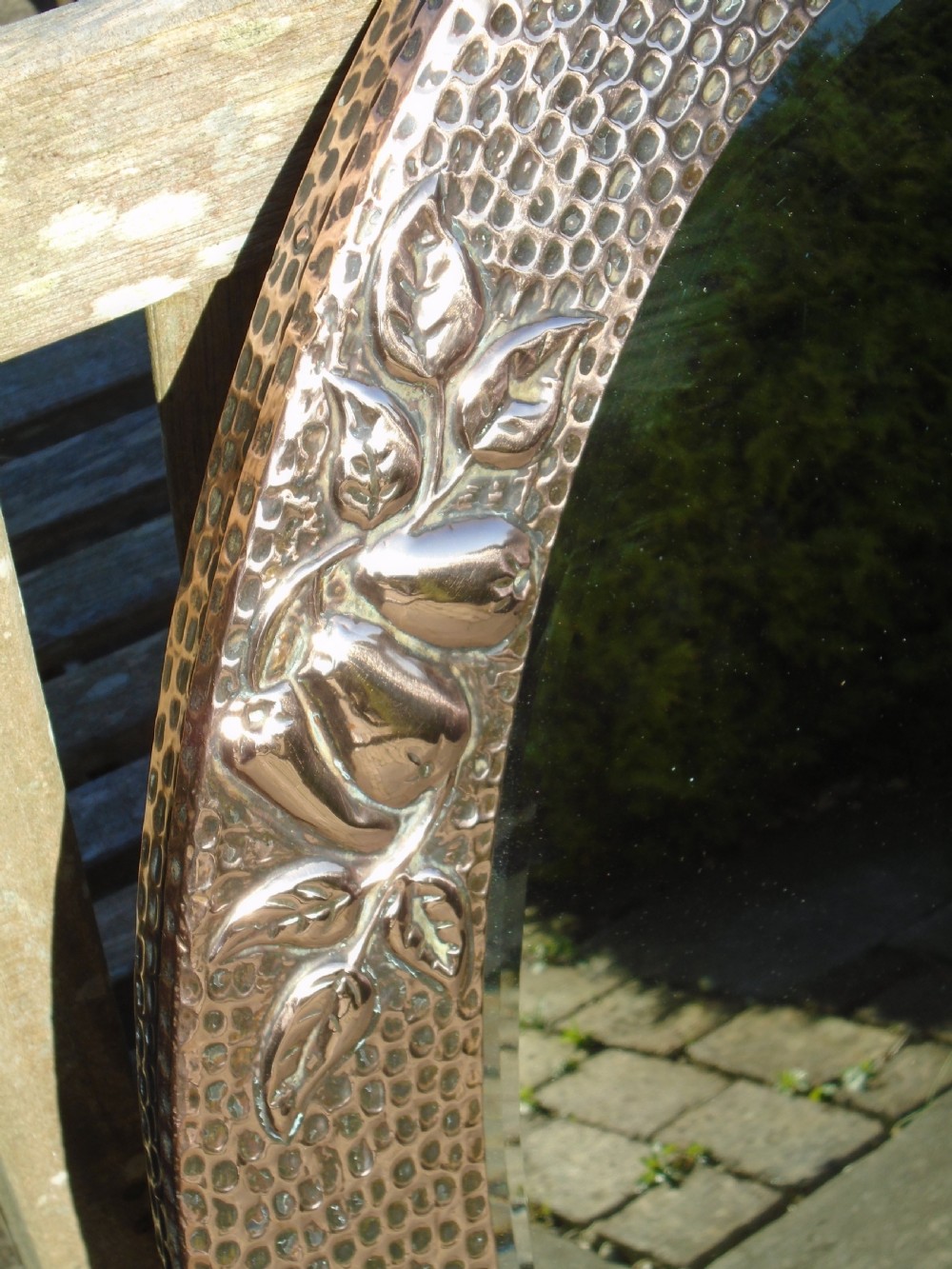 An oval Arts and Crafts mirror featuring a hand-hammered copper frame decorated with embossed pear motifs and decorative raised cabochons. View IV