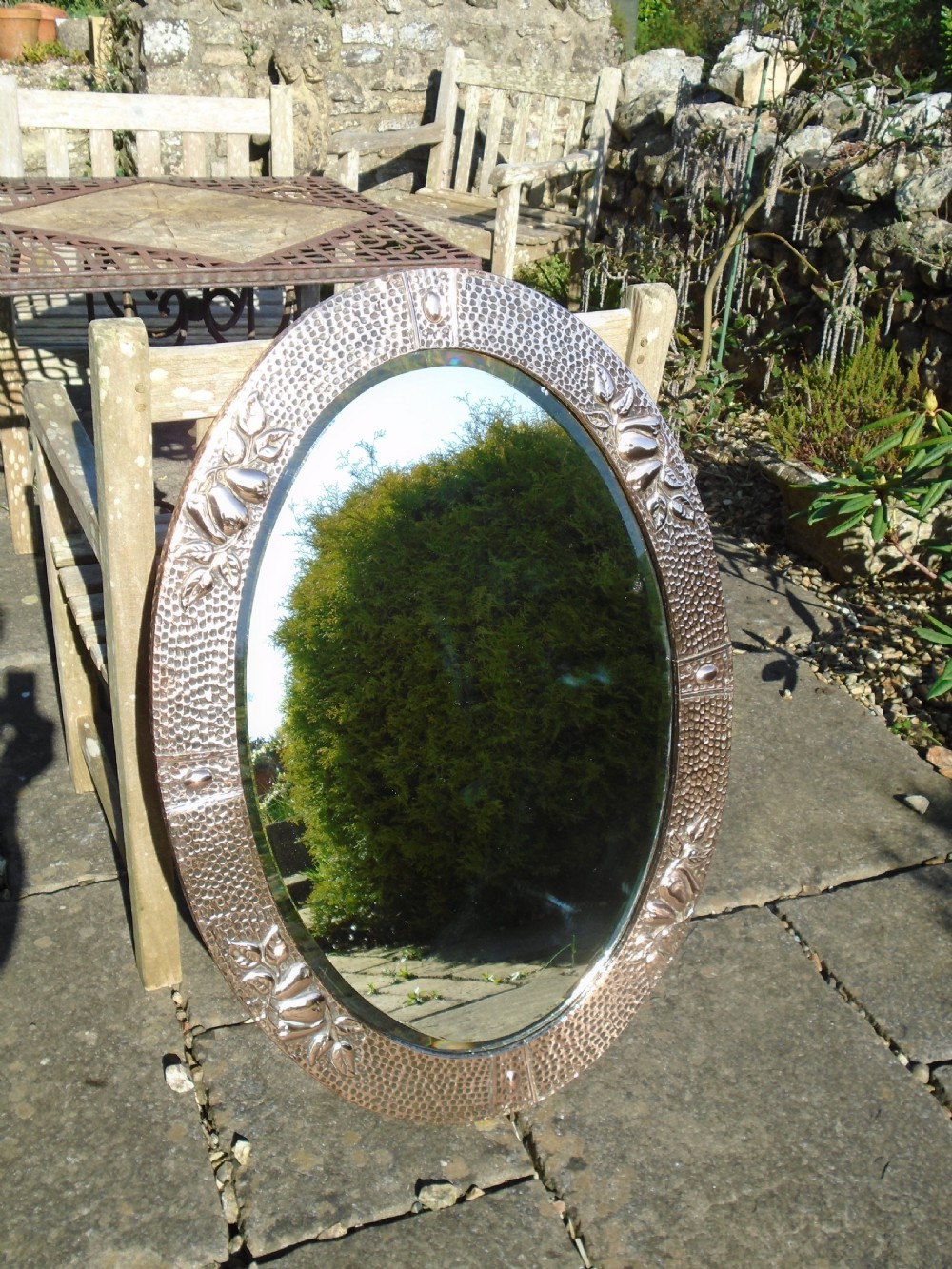 An oval Arts and Crafts mirror featuring a hand-hammered copper frame decorated with embossed pear motifs and decorative raised cabochons. View V
