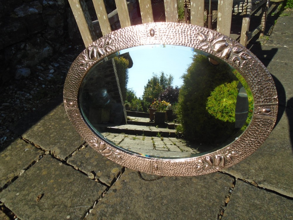 An oval Arts and Crafts mirror featuring a hand-hammered copper frame decorated with embossed pear motifs and decorative raised cabochons. View IX