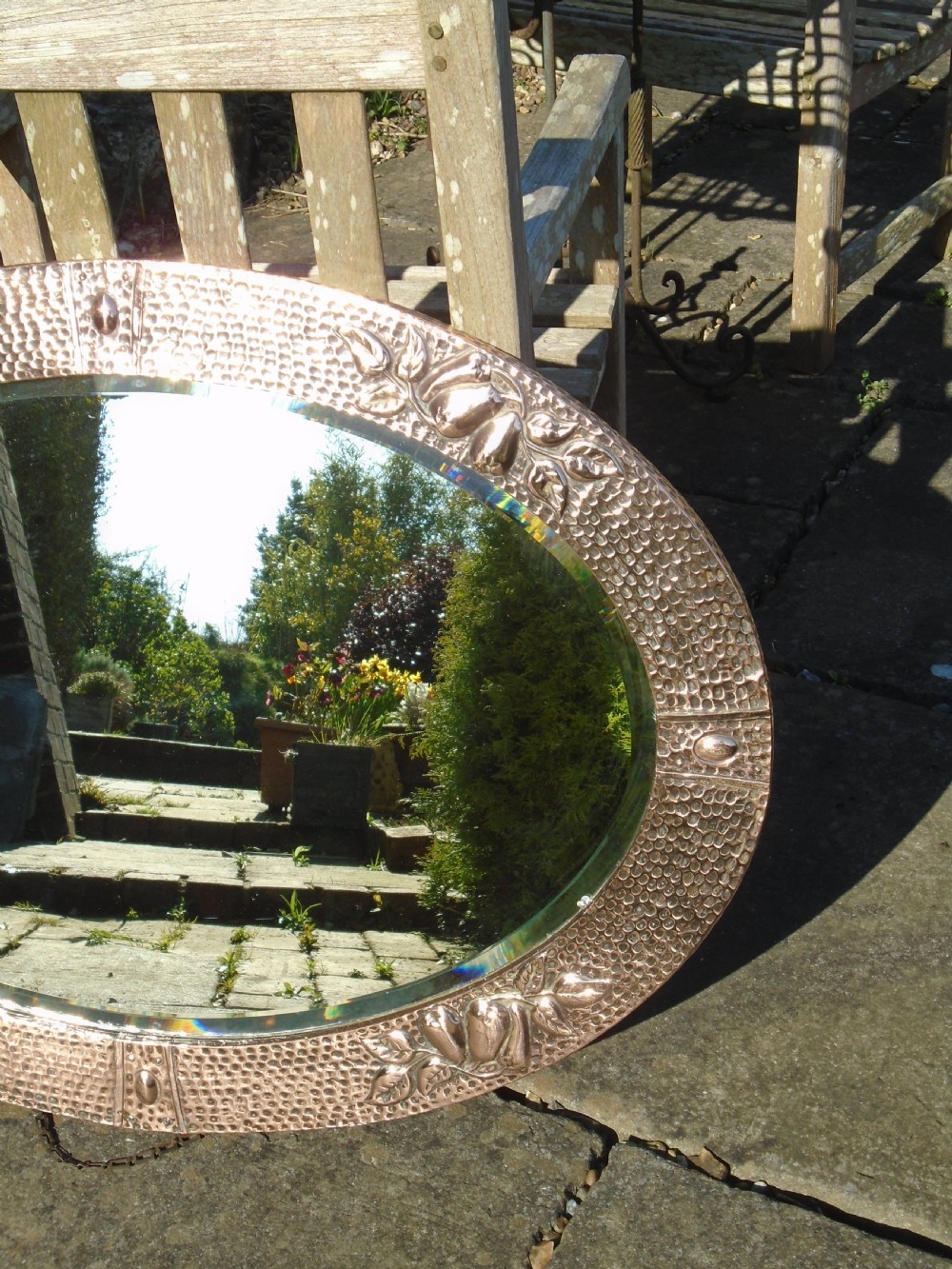 An oval Arts and Crafts mirror featuring a hand-hammered copper frame decorated with embossed pear motifs and decorative raised cabochons. View X