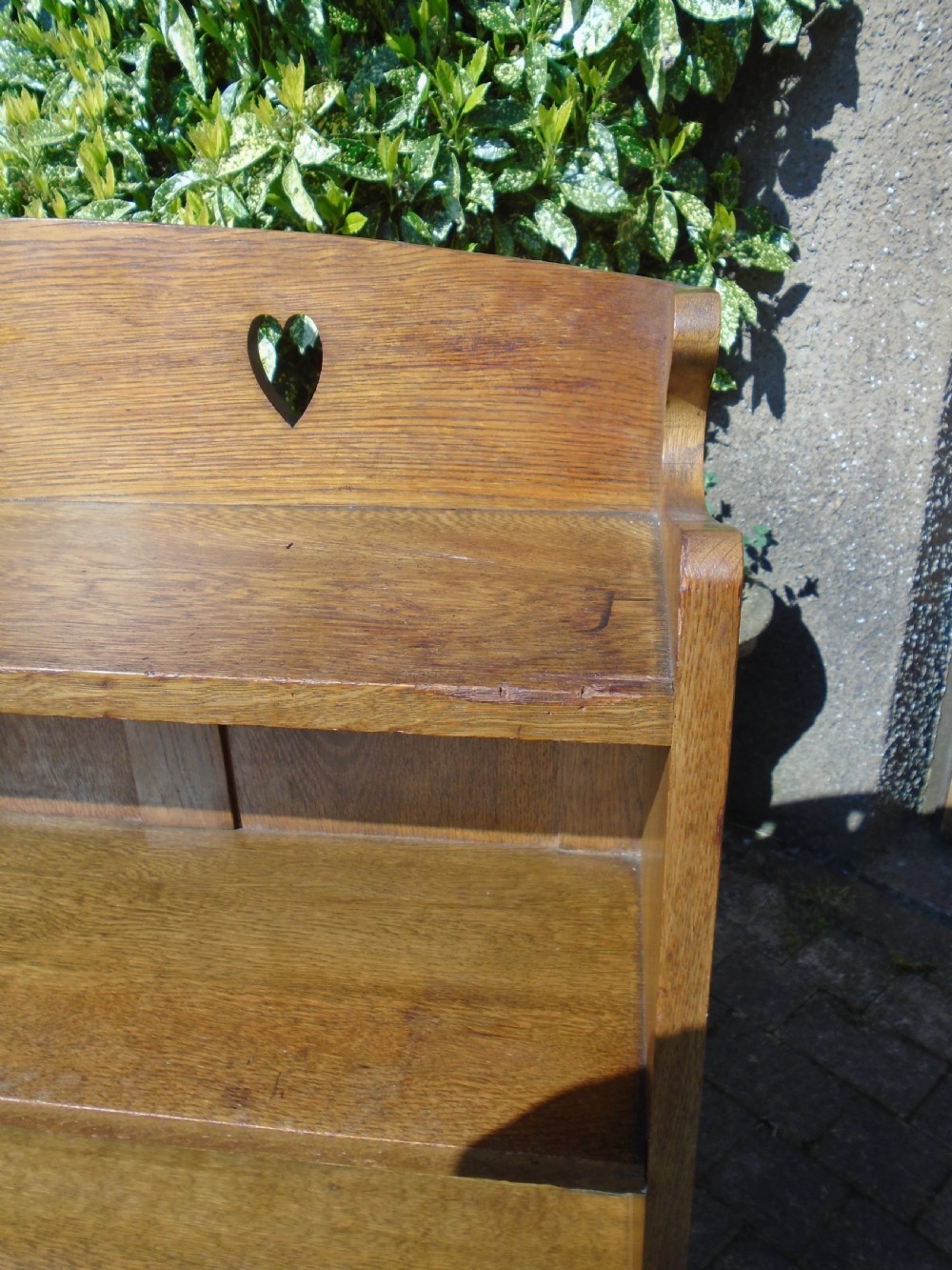 A freestanding Arts and Crafts medium oak open bookcase featuring four shelves, a shaped top gallery with cut-out heart motifs, and cut-out heart details on the base sides. View V