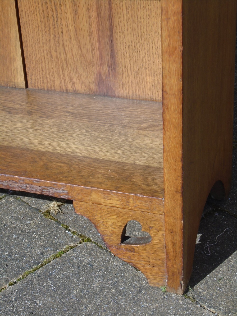 A freestanding Arts and Crafts medium oak open bookcase featuring four shelves, a shaped top gallery with cut-out heart motifs, and cut-out heart details on the base sides. View VIII