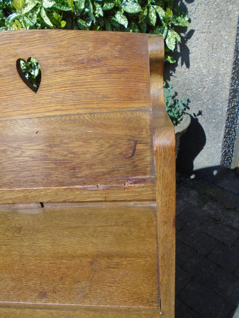 A freestanding Arts and Crafts medium oak open bookcase featuring four shelves, a shaped top gallery with cut-out heart motifs, and cut-out heart details on the base sides. View IX