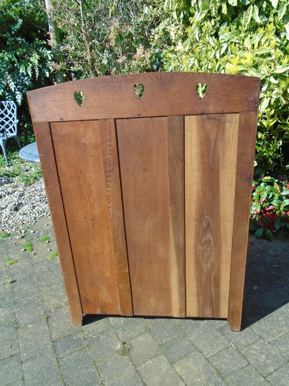 A freestanding Arts and Crafts medium oak open bookcase featuring four shelves, a shaped top gallery with cut-out heart motifs, and cut-out heart details on the base sides. View X