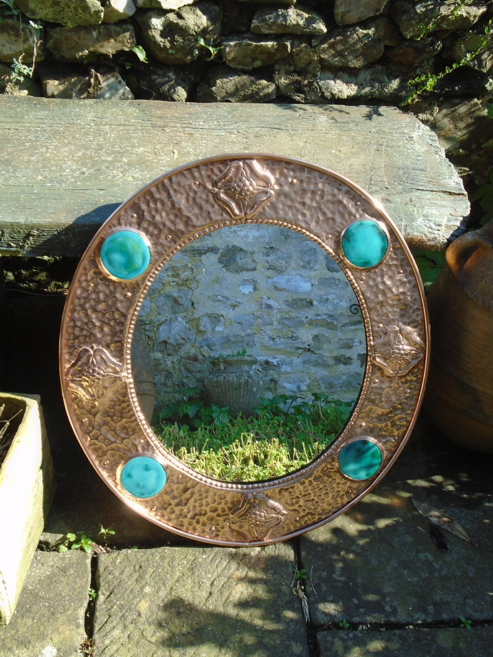 An oval Arts and Crafts wall mirror featuring a hand-hammered copper frame decorated with repousse floral motifs and four turquoise round cabochons. View II